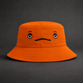 Orange bucket hat with a face design on a gray background inspired by Sassy from the Big Lez Show